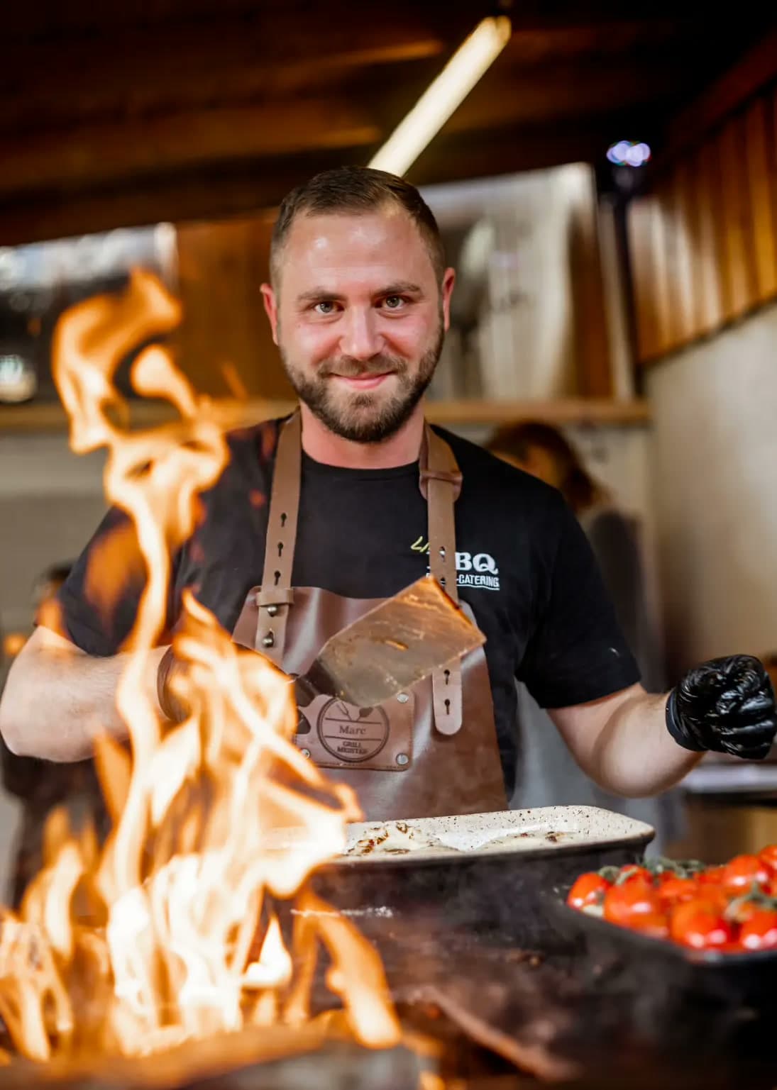Marc Neugebauer lächelt am Grill, vor ihm lodert das Feuer
